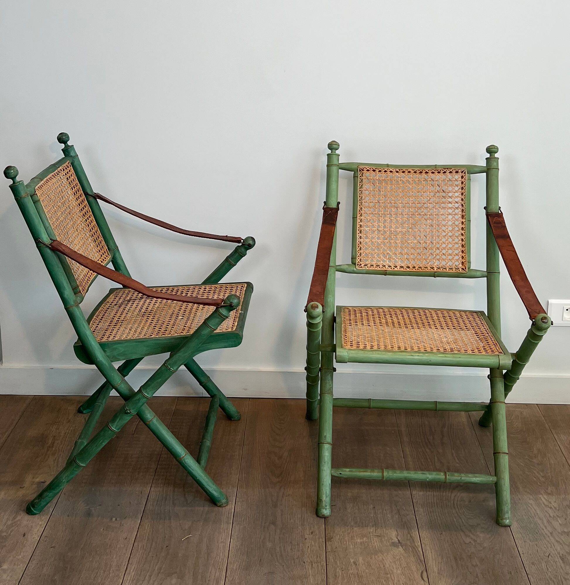 Paire de chaises safari pliantes façon faux-bambou patiné, dossiers et assises cannées et repose-bras en cuir