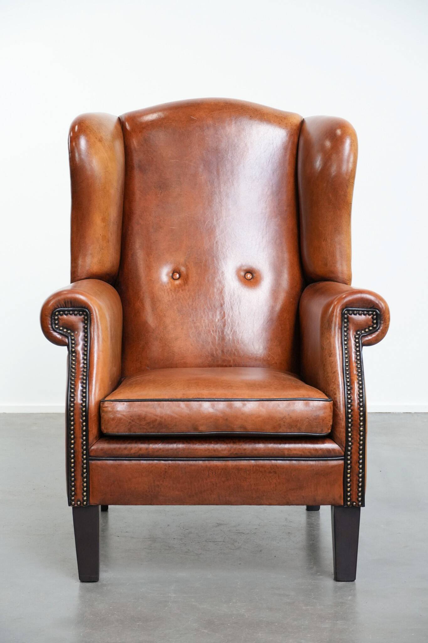 Large sheepskin wingback chair with black piping and decorative nails