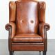 Large sheepskin wingback chair with black piping and decorative nails