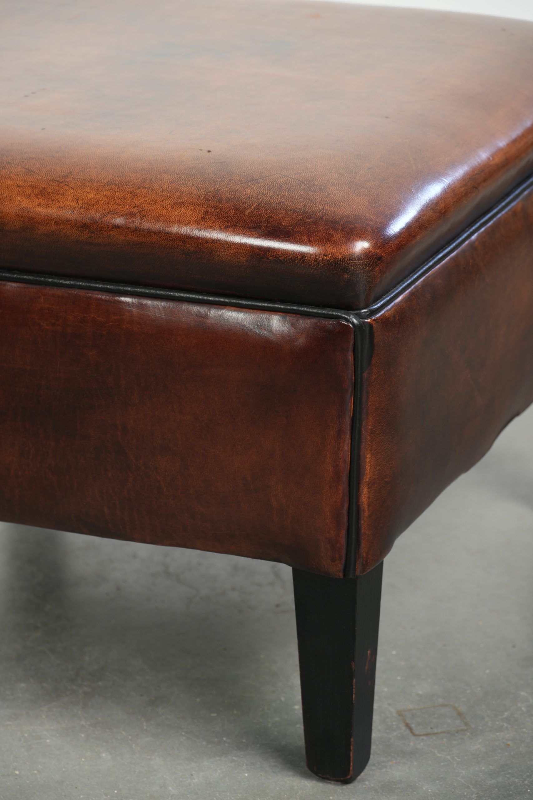 Large dark brown square ottoman made of sheepskin with black piping