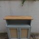 Small vintage green-grey piece of furniture, with 2 doors covered in burlap.