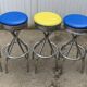 Set of 5 vintage swivel bar stools in blue, red, orange, and yellow.
