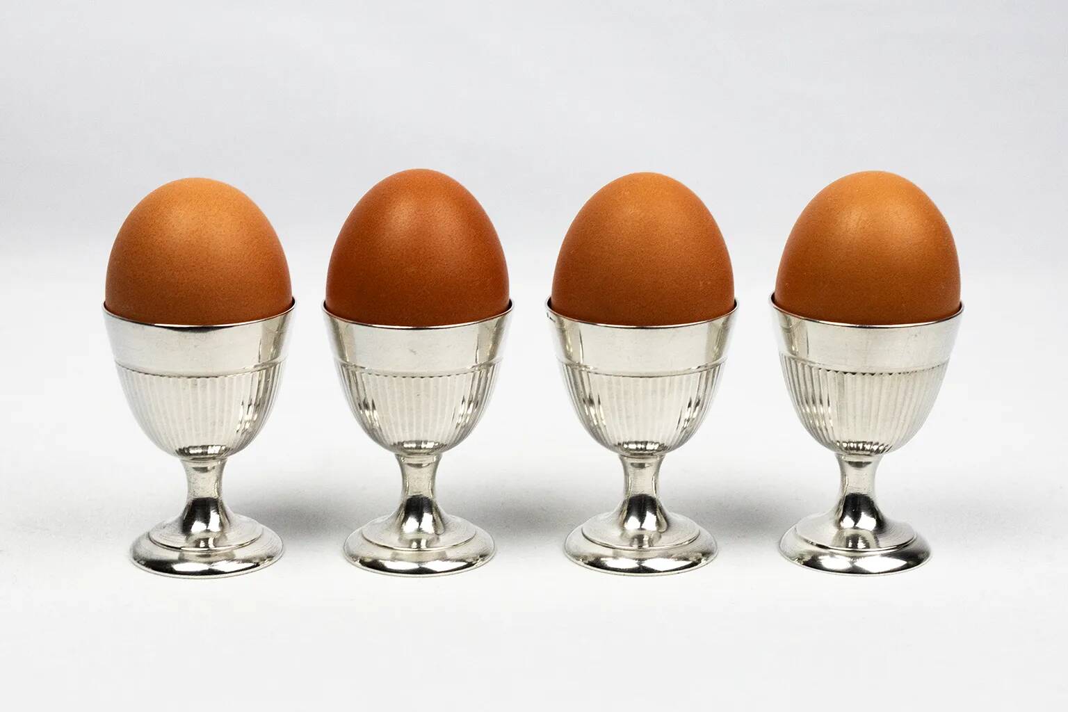 Four silver-plated Christofle egg cups with fluted sides.