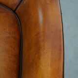 Cognac-colored sheepskin armchair with black piping and decorative nails