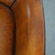 Cognac-colored sheepskin armchair with black piping and decorative nails