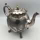 Old teapot pourer in silver metal decorated with foliage and butterflies