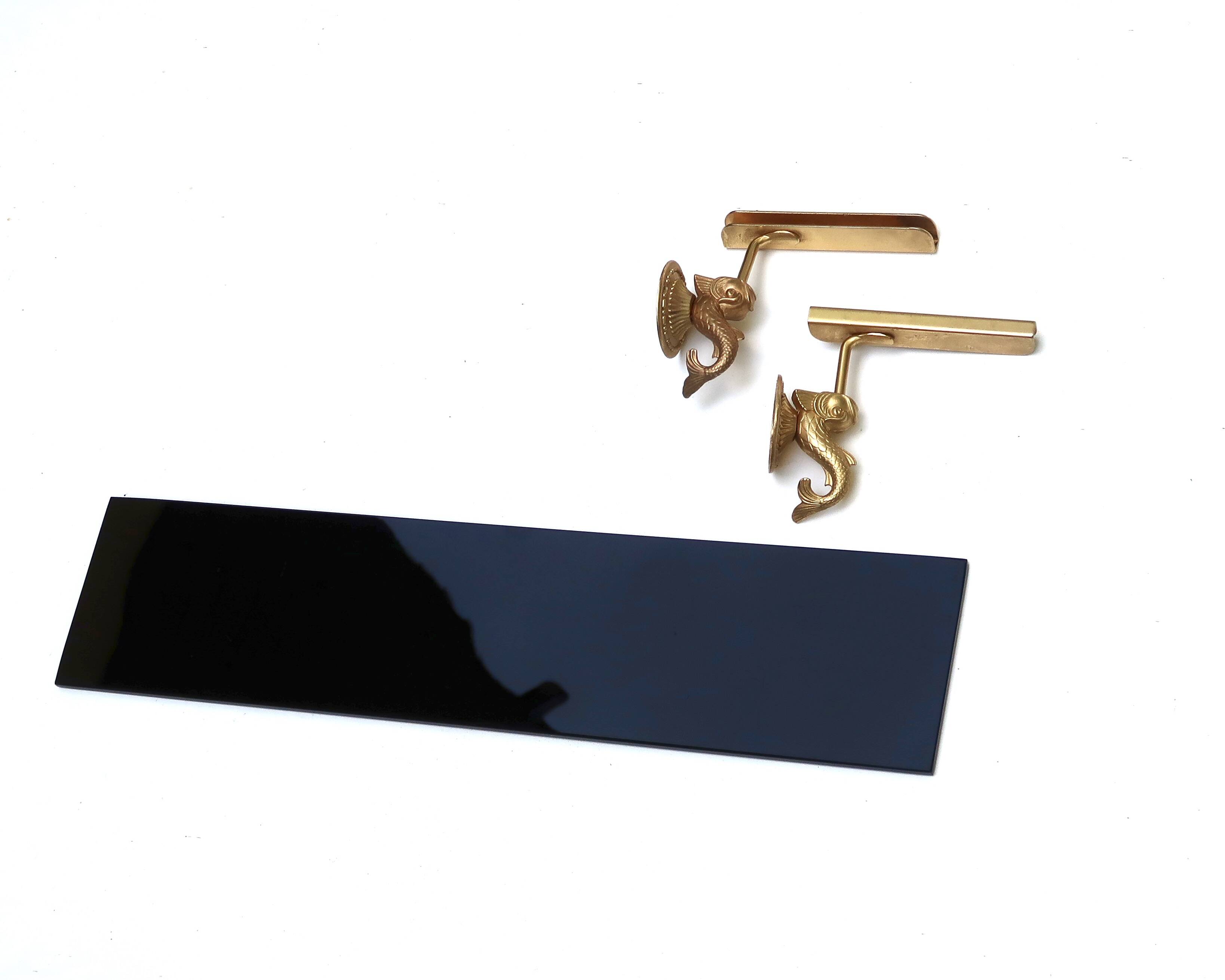 Wall shelf in gold metal and black glass adorned with fish.