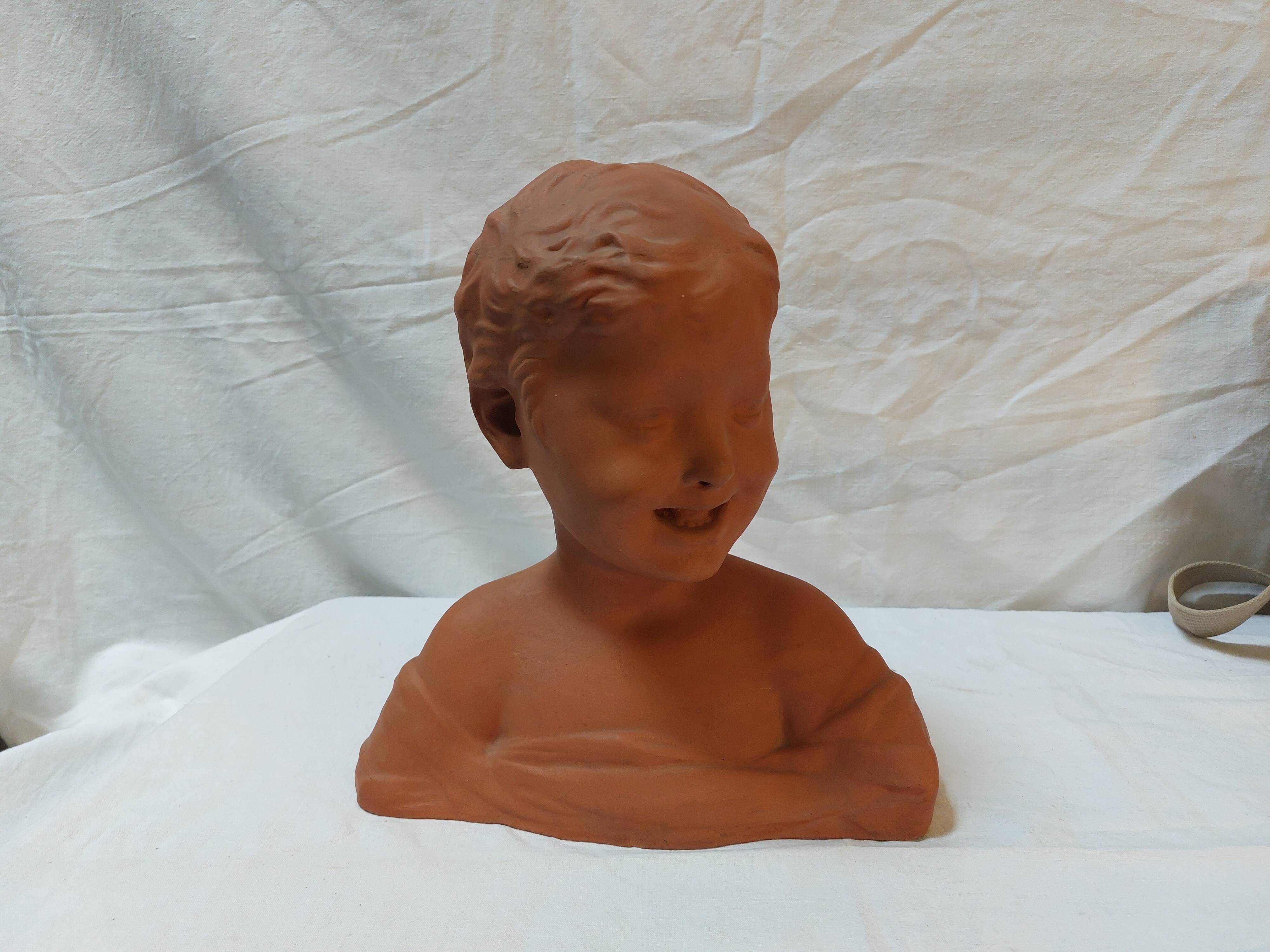 Terracotta bust of a smiling little boy.
