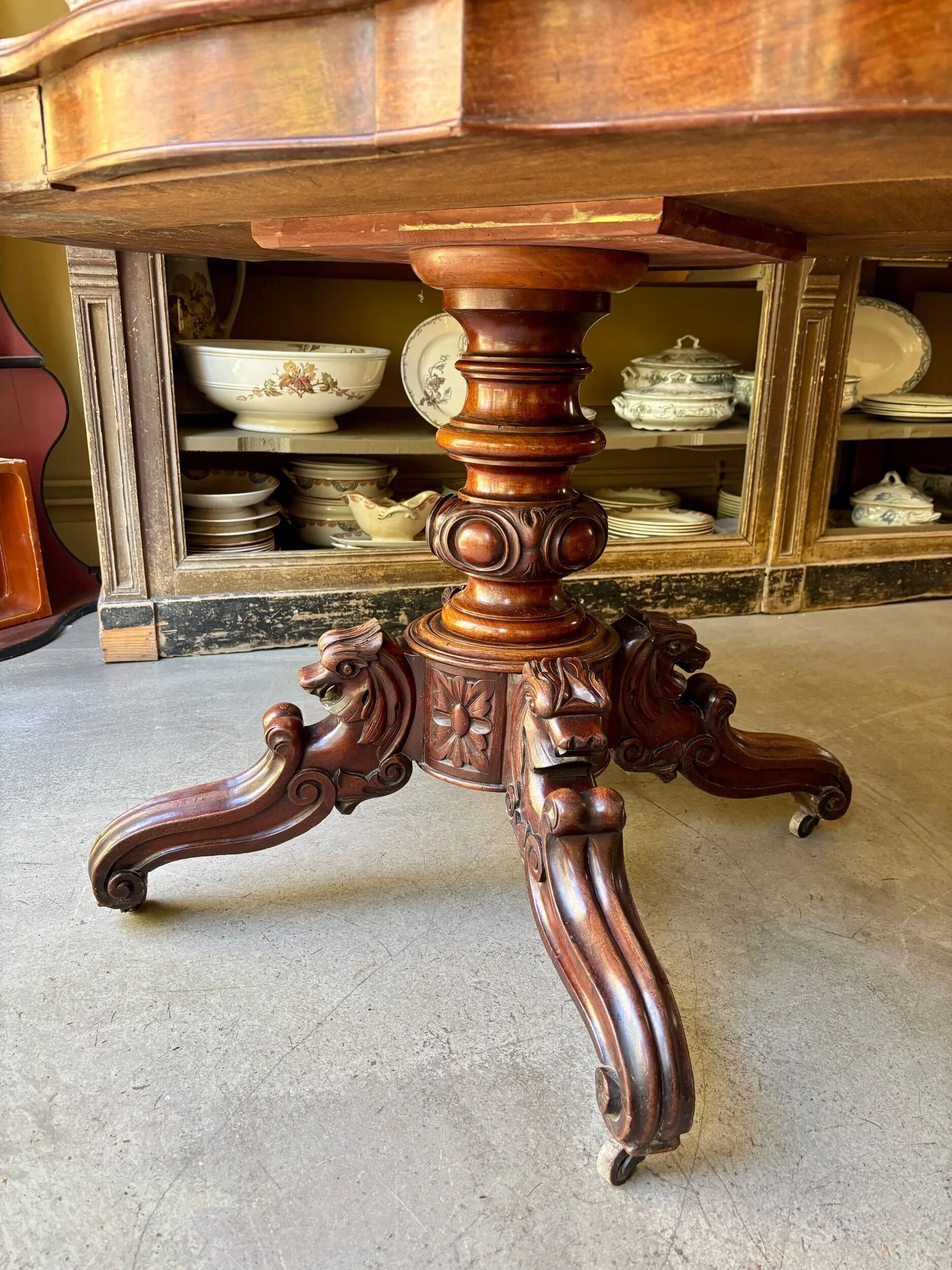 Table with a carved wooden frame and grey marble top on wheels, measuring 130 x 82 cm.