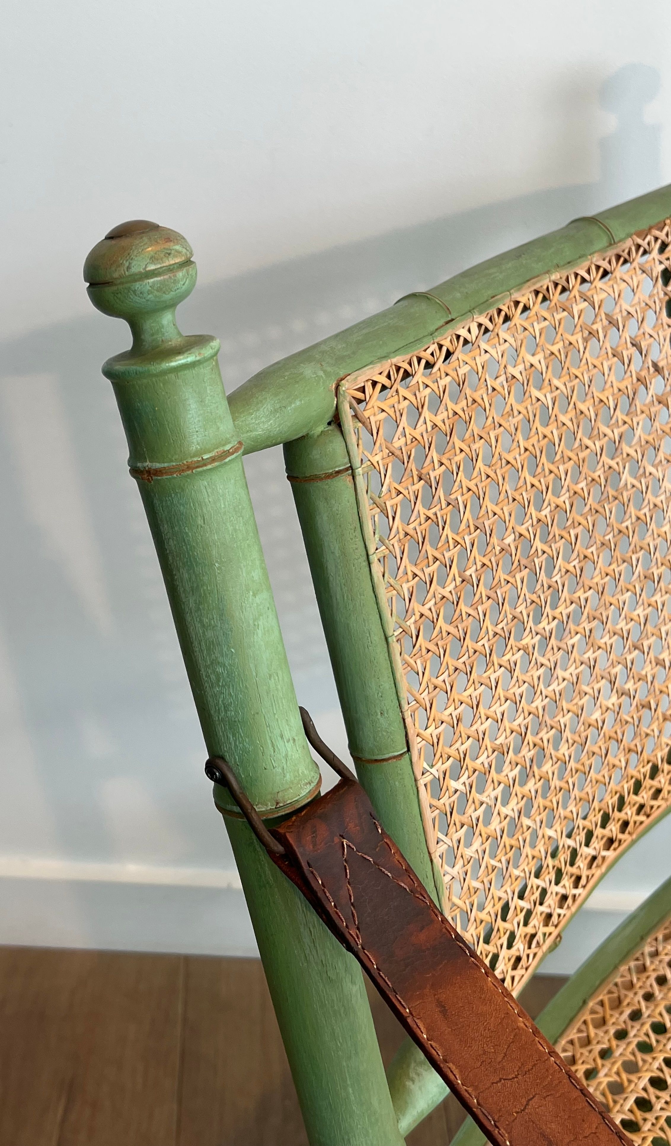 Paire de chaises safari pliantes façon faux-bambou patiné, dossiers et assises cannées et repose-bras en cuir