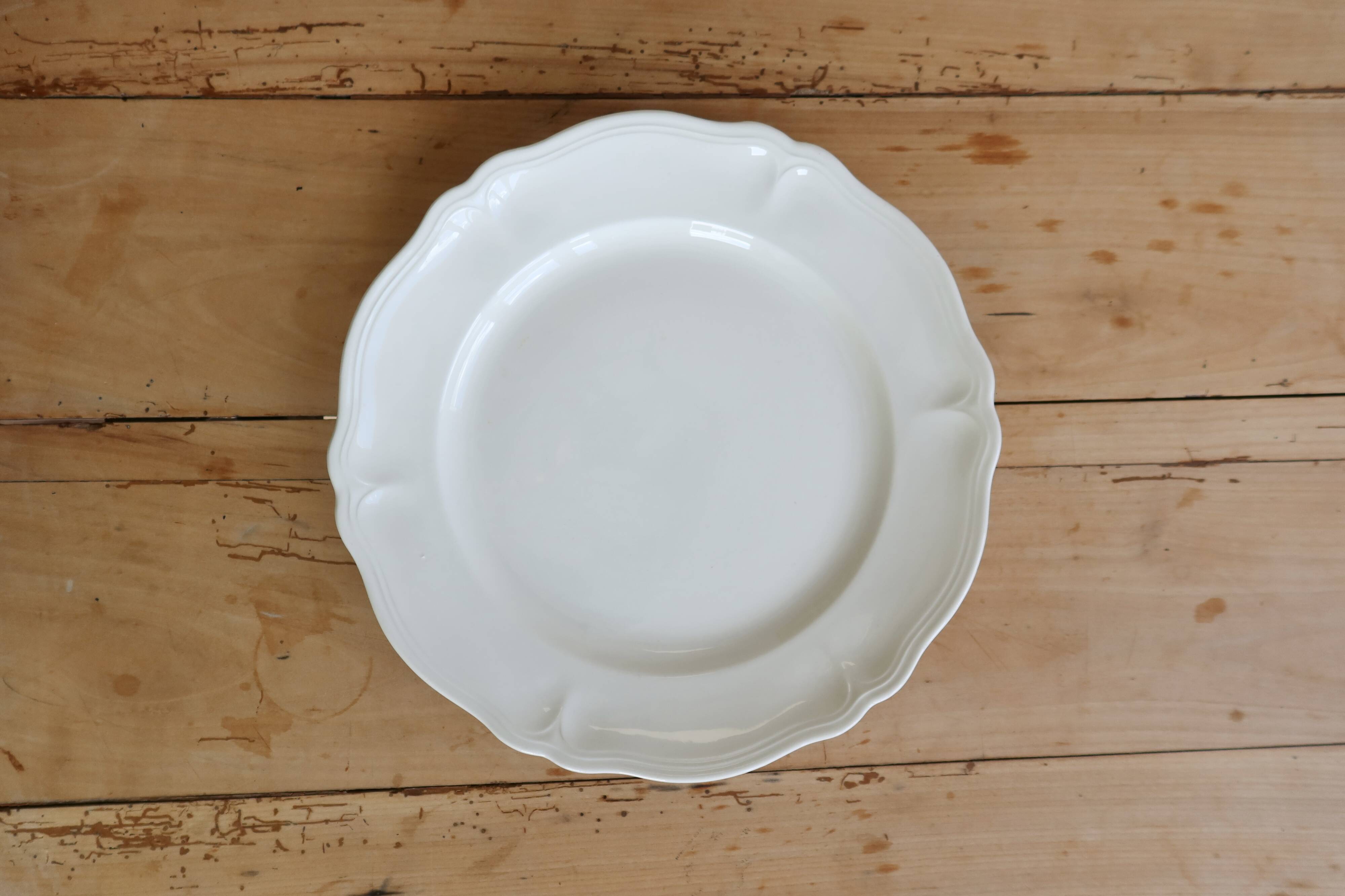 Round vintage ivory earthenware serving dish with scalloped rim.