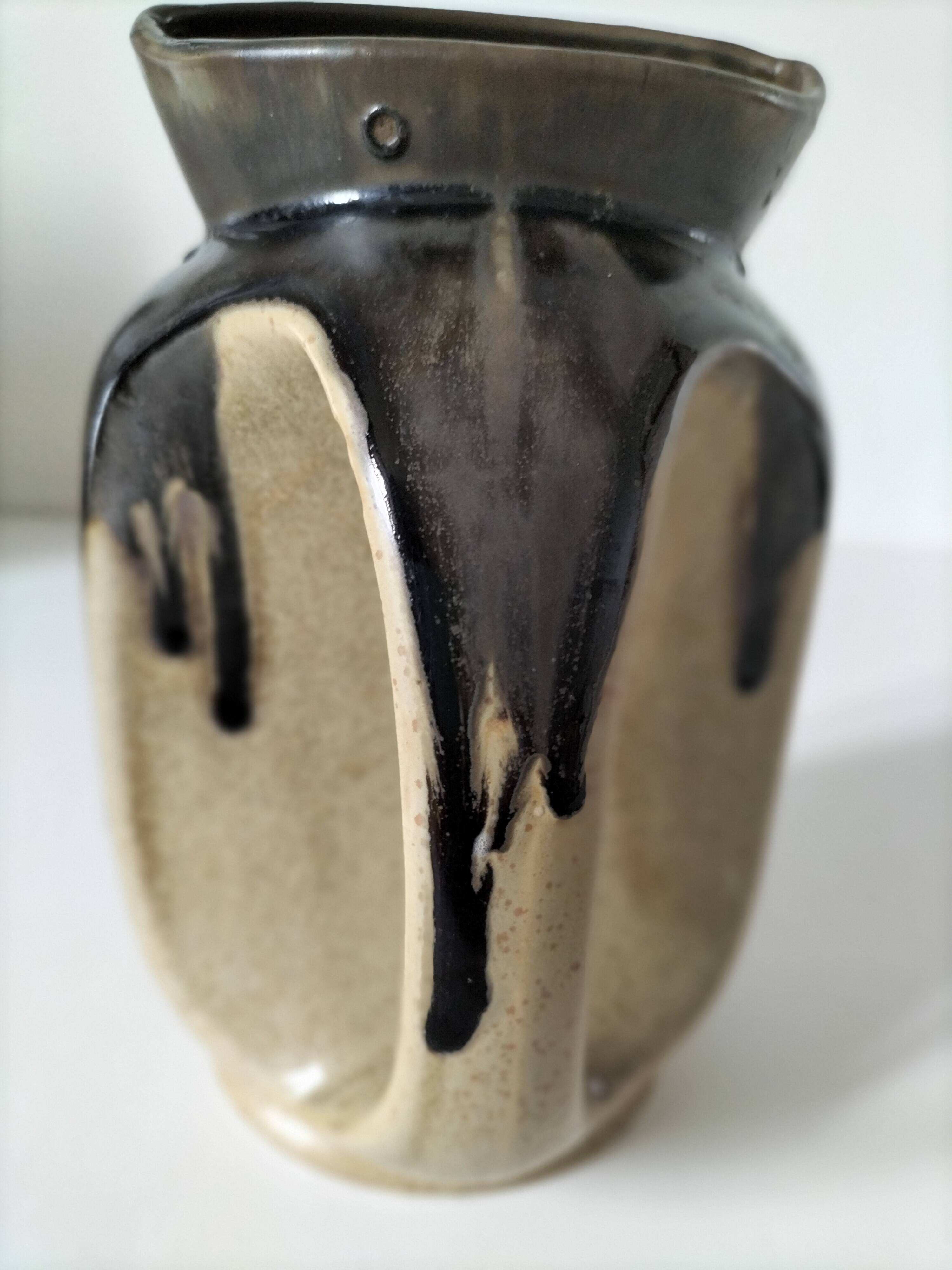Stoneware jug with deep black drips on a sandy background.