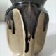 Stoneware jug with deep black drips on a sandy background.