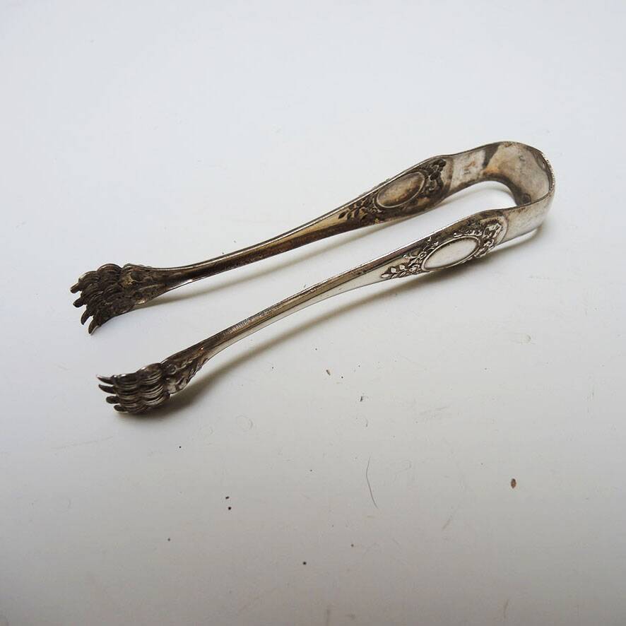 Antique metal sugar tongs in the shape of a lion's paw.