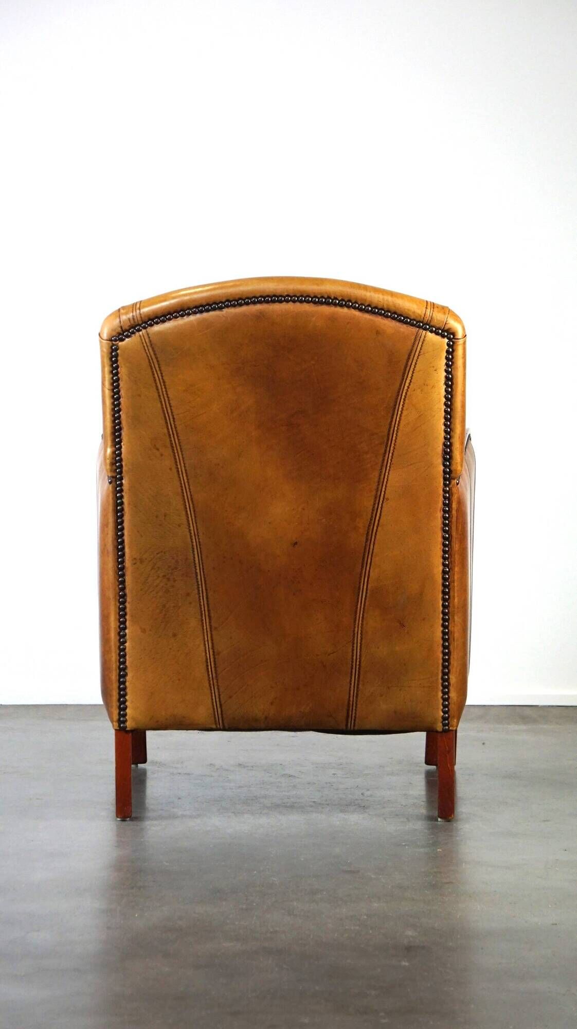 Luxurious cowhide Art Deco design armchair with wooden armrests and cognac-colored leather