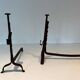 Pair of wrought iron andirons with adjustable supports and tripod feet.