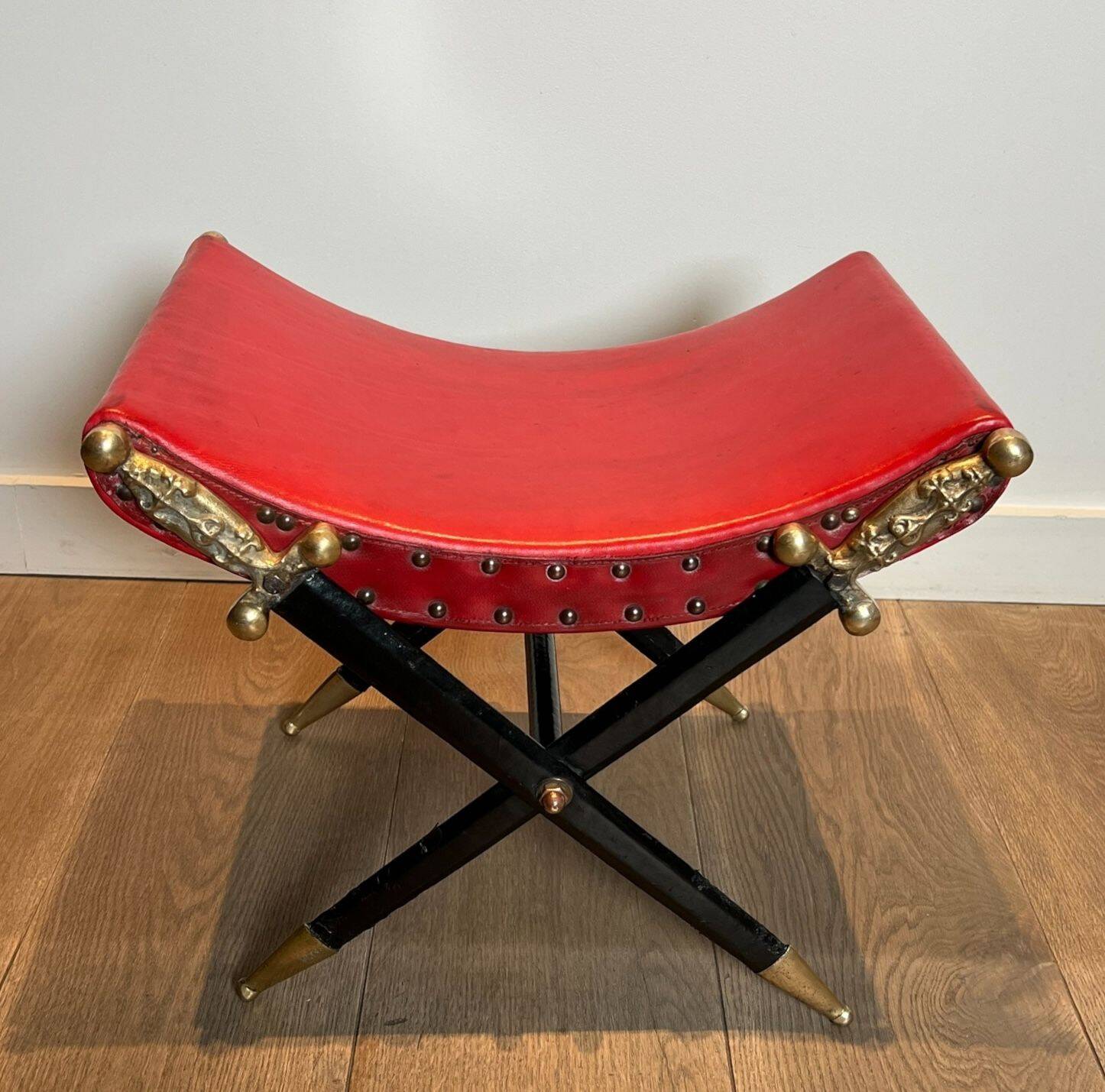 Neoclassical curule stool in red leather, decorated with crossed swords in bronze and metal covered in black leather.