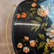 Large vintage 1960s platter with floral decoration on a black background and golden handles.
