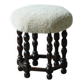 Mid-Century Modern style stool, in dark stained wood, with a lambswool seat and spool-shaped legs, 1950s.