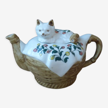 Théière chat en porcelaine allongé sur une couverture dans un panier