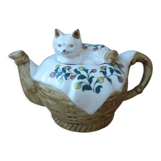 Porcelain cat teapot lying on a blanket in a basket