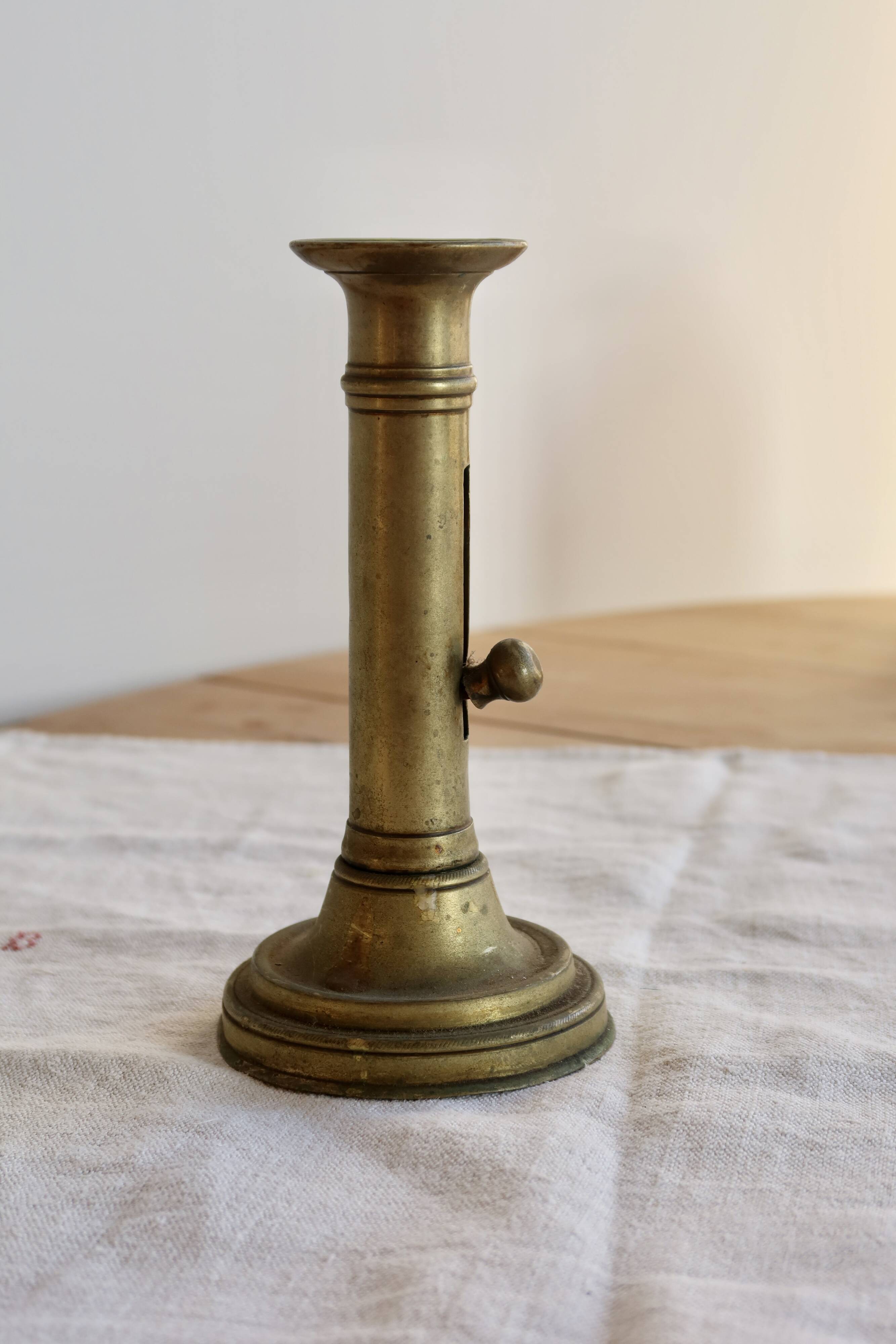 Antique brass candlestick with a push button.