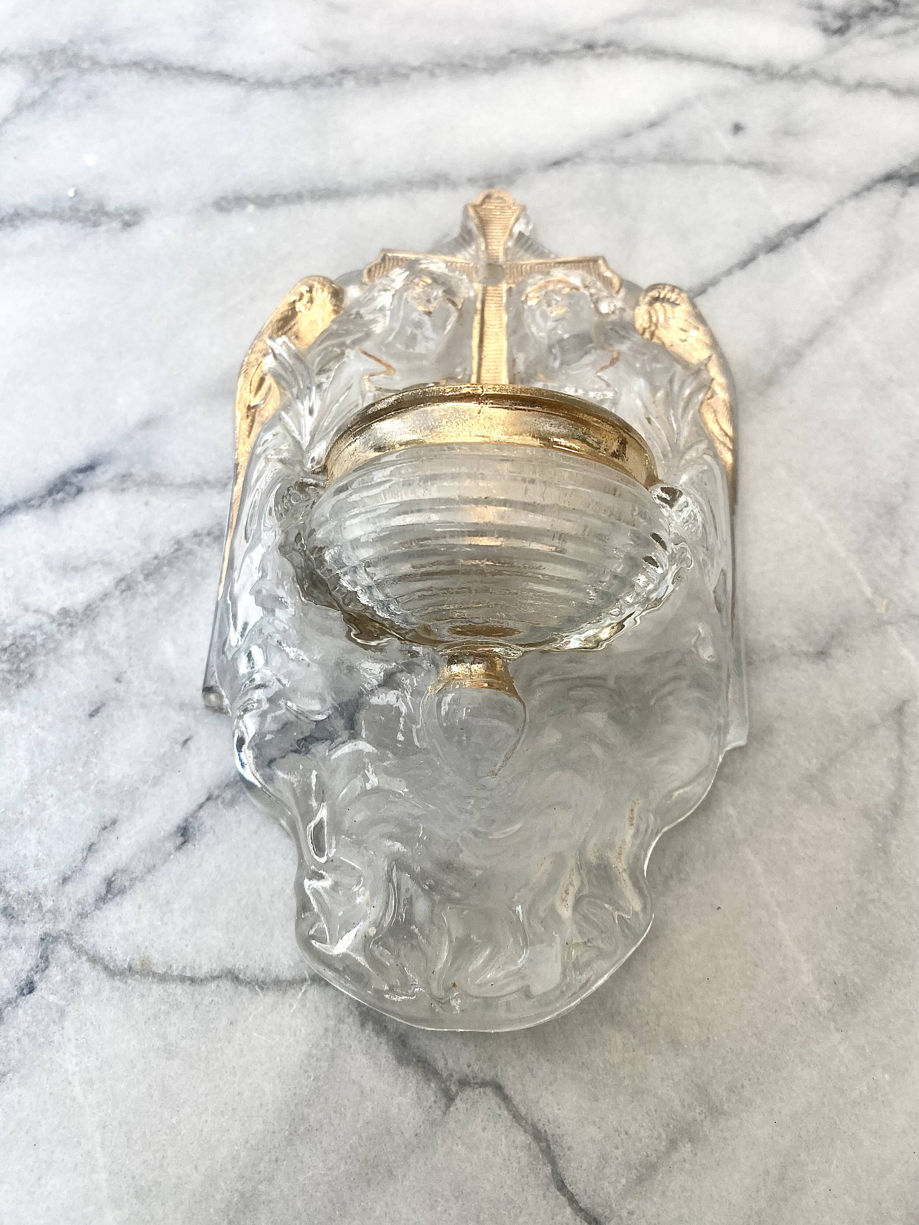 Old wall-mounted holy water font in moulded glass decorated with angels.