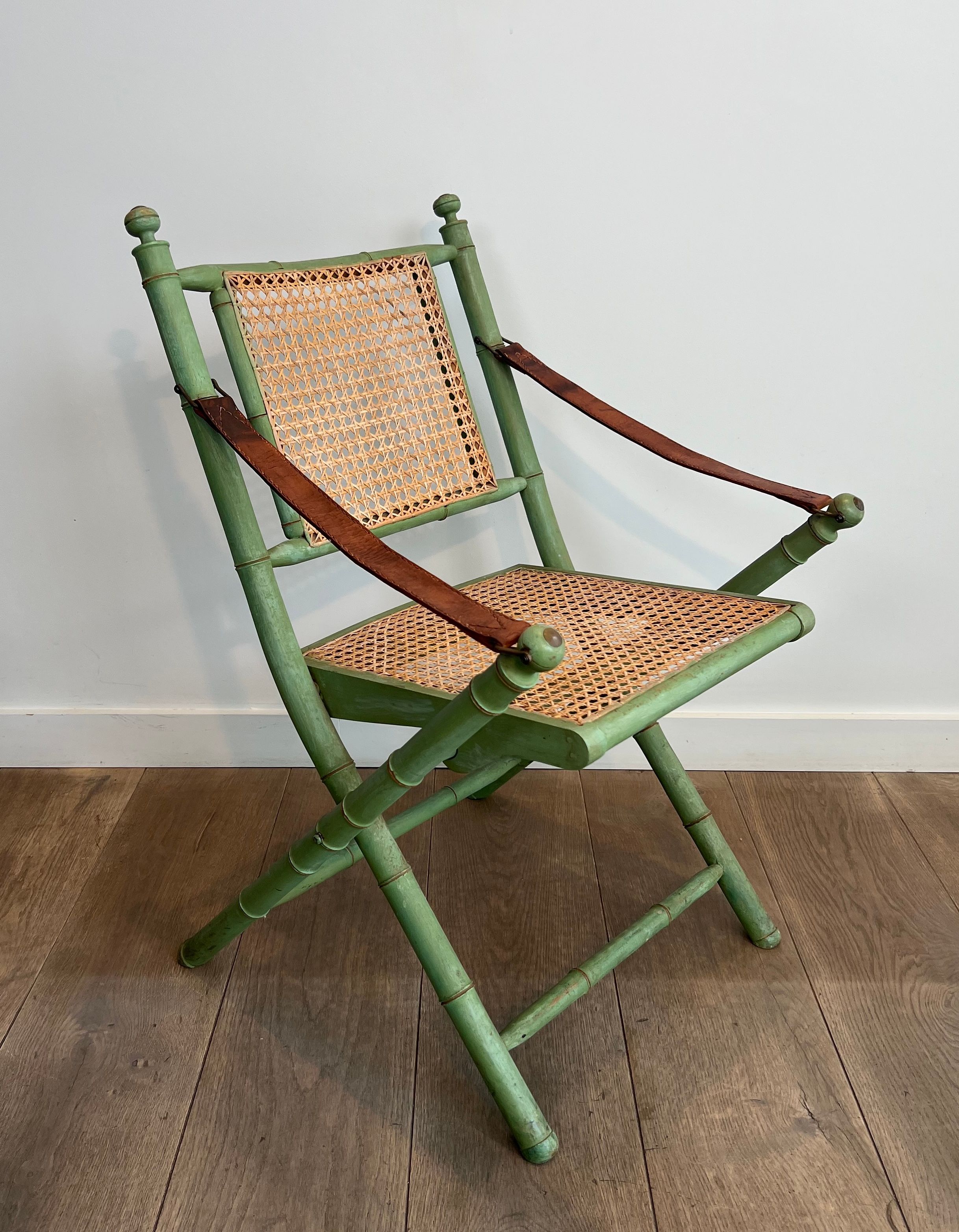 Paire de chaises safari pliantes façon faux-bambou patiné, dossiers et assises cannées et repose-bras en cuir