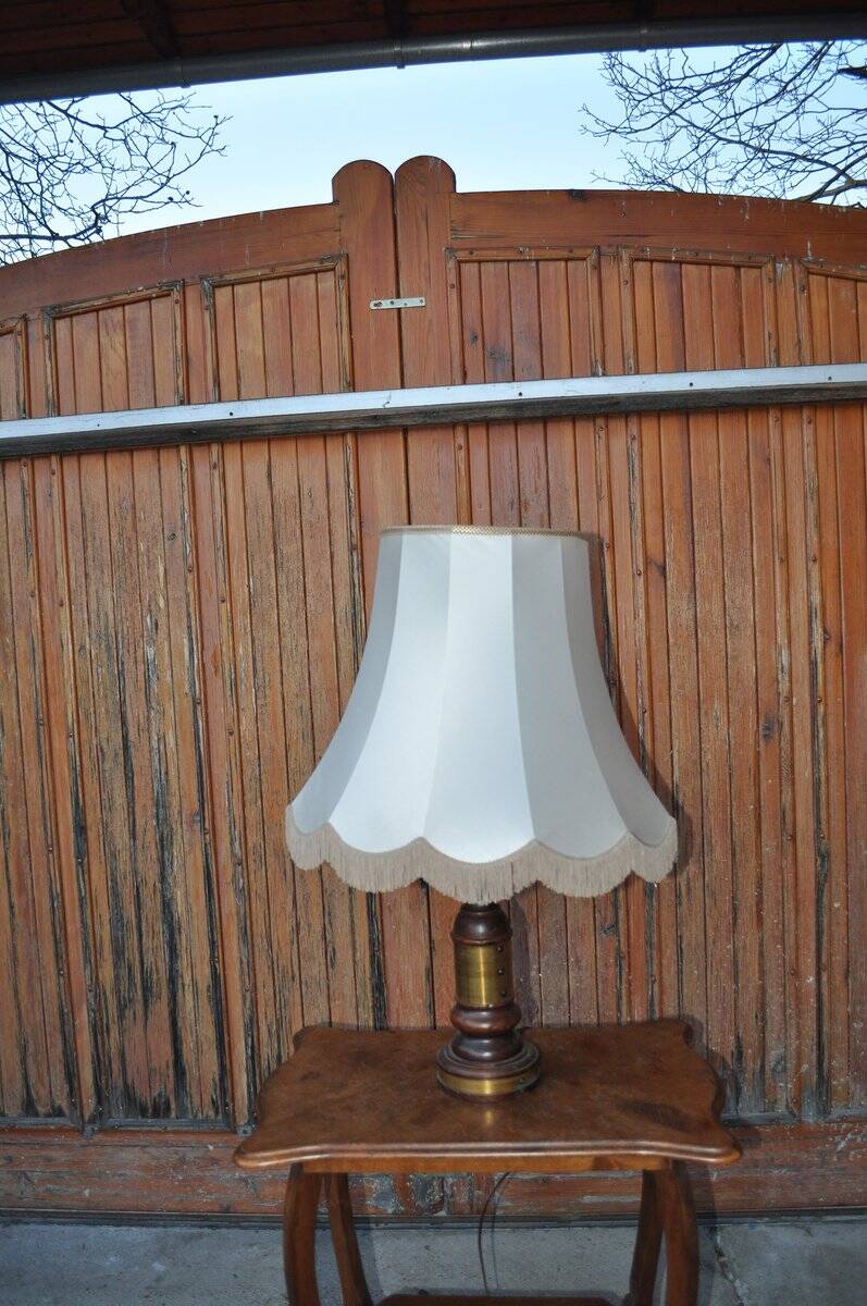 Vintage brown and gold desk lamp made of carved wood and brass, with a fringed shade.