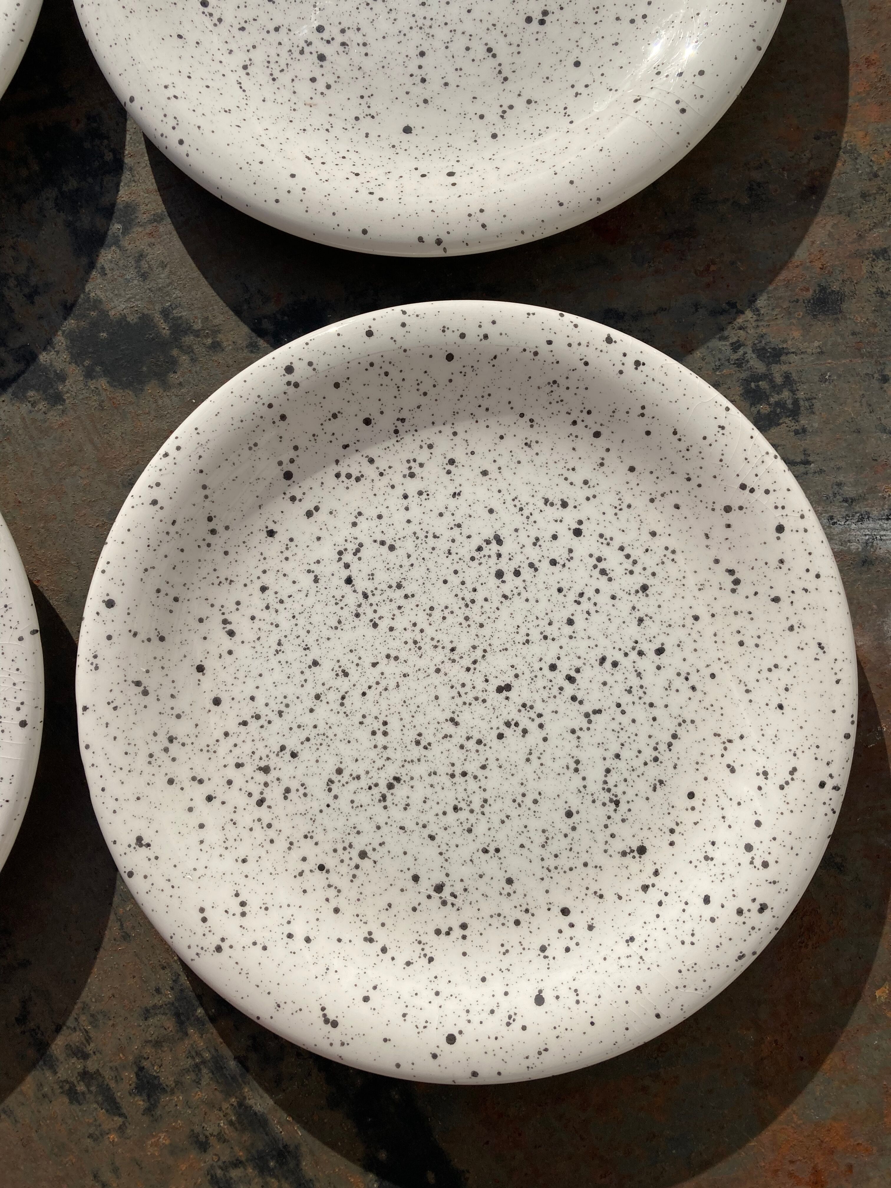 4 black speckled dessert plates on a vintage white background