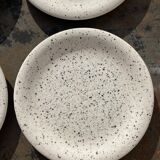 4 black speckled dessert plates on a vintage white background