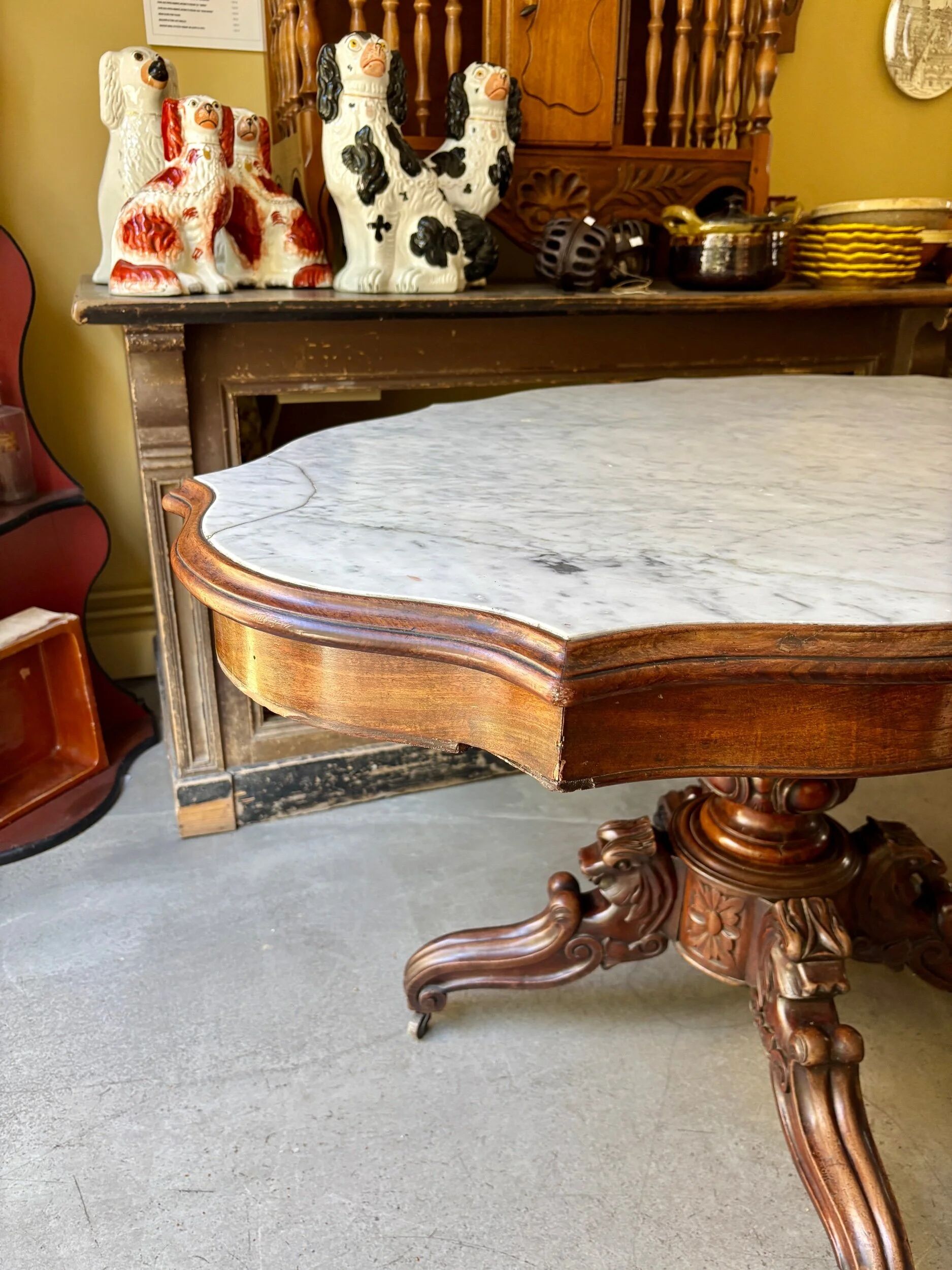 Table with a carved wooden frame and grey marble top on wheels, measuring 130 x 82 cm.