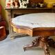 Table with a carved wooden frame and grey marble top on wheels, measuring 130 x 82 cm.