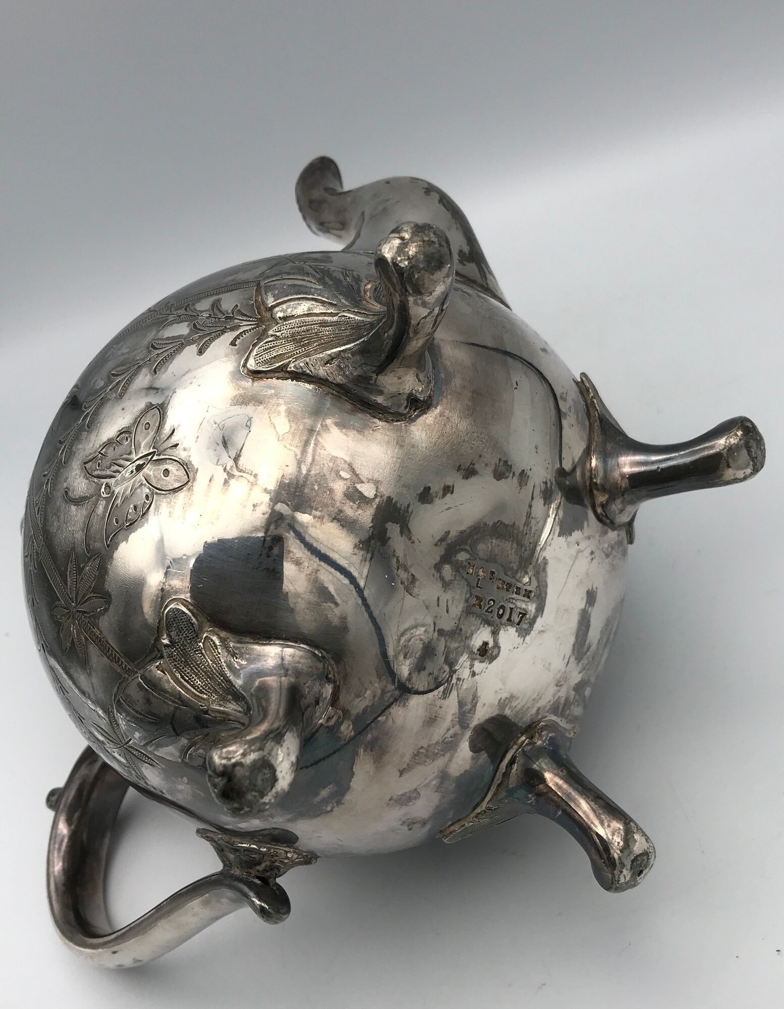 Old teapot pourer in silver metal decorated with foliage and butterflies