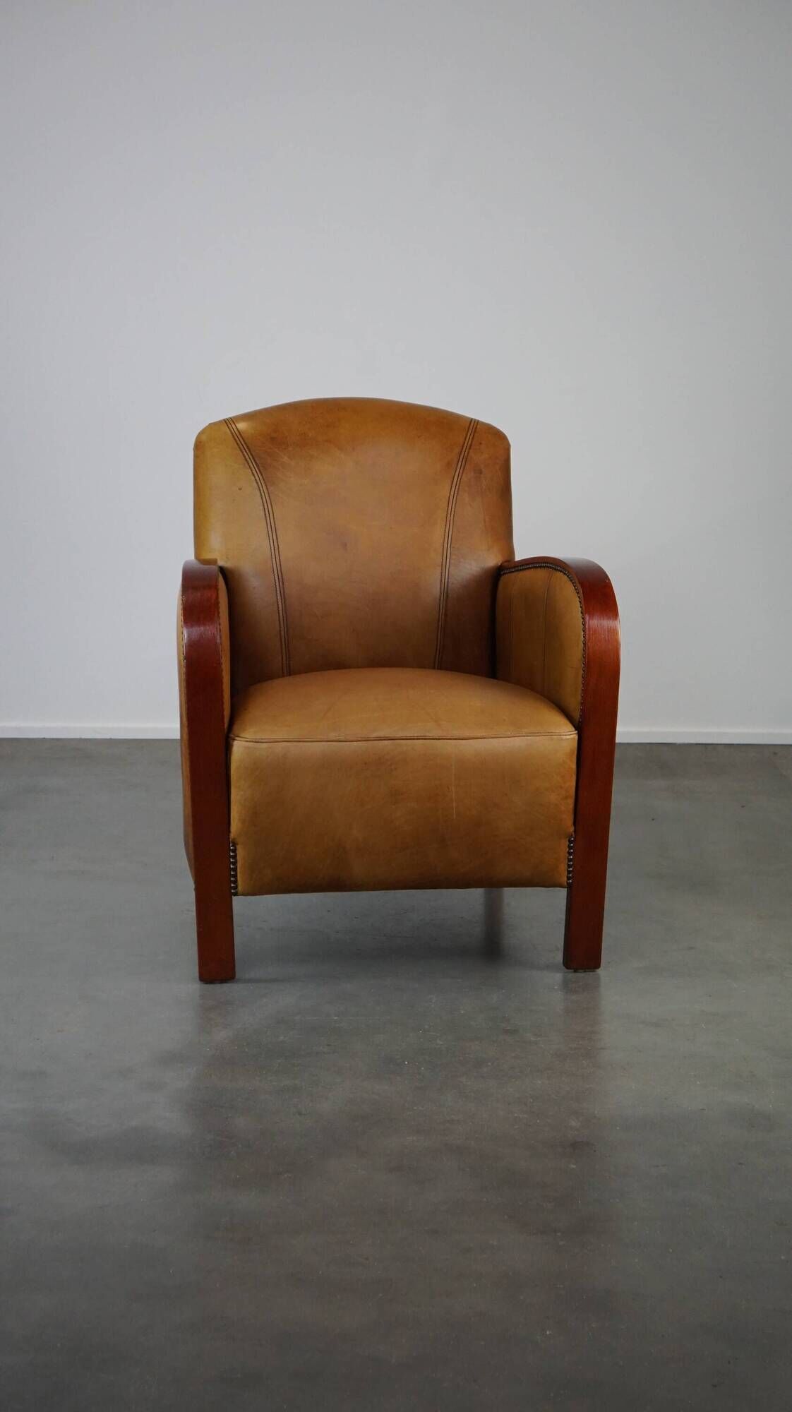 Luxurious cowhide Art Deco design armchair with wooden armrests and cognac-colored leather