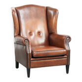 Fauteuil à oreilles en peau de mouton de couleur cognac chaude avec des clous raffinés.