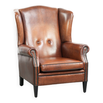 Sheepskin wingback armchair in a warm cognac colour with refined nailhead trim