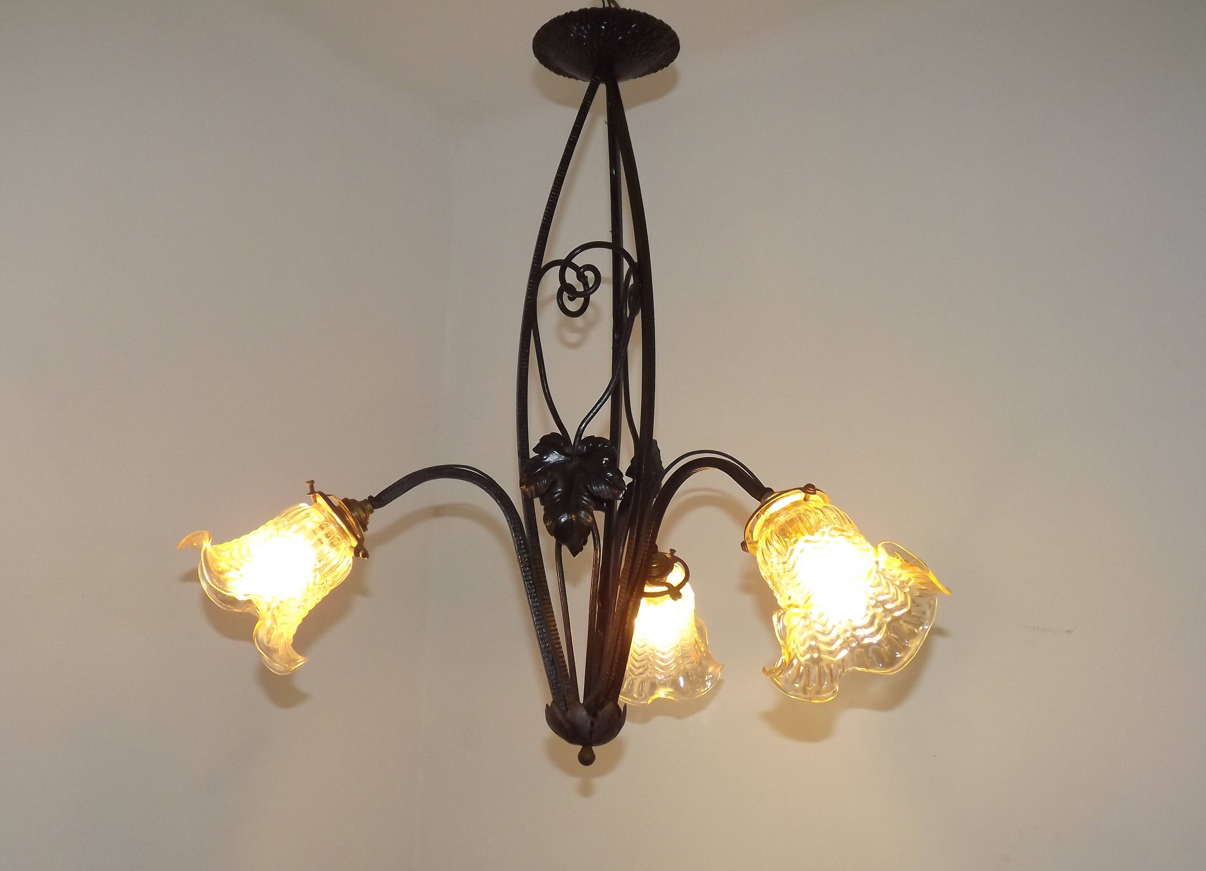 French Art Nouveau leaf detail iron three-light chandelier with amber glass shades.