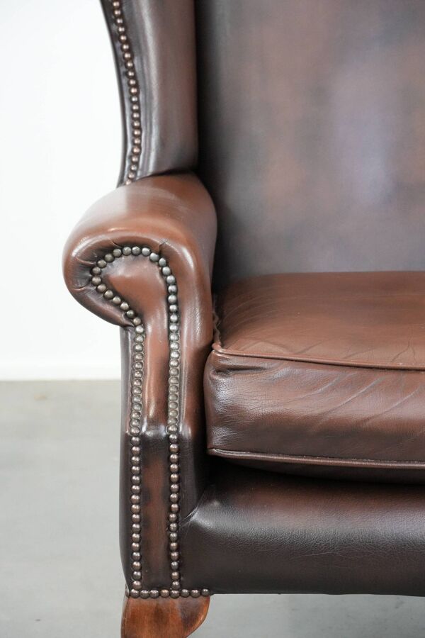 Fauteuil à oreilles Chesterfield en cuir lisse marron dans le style anglais.