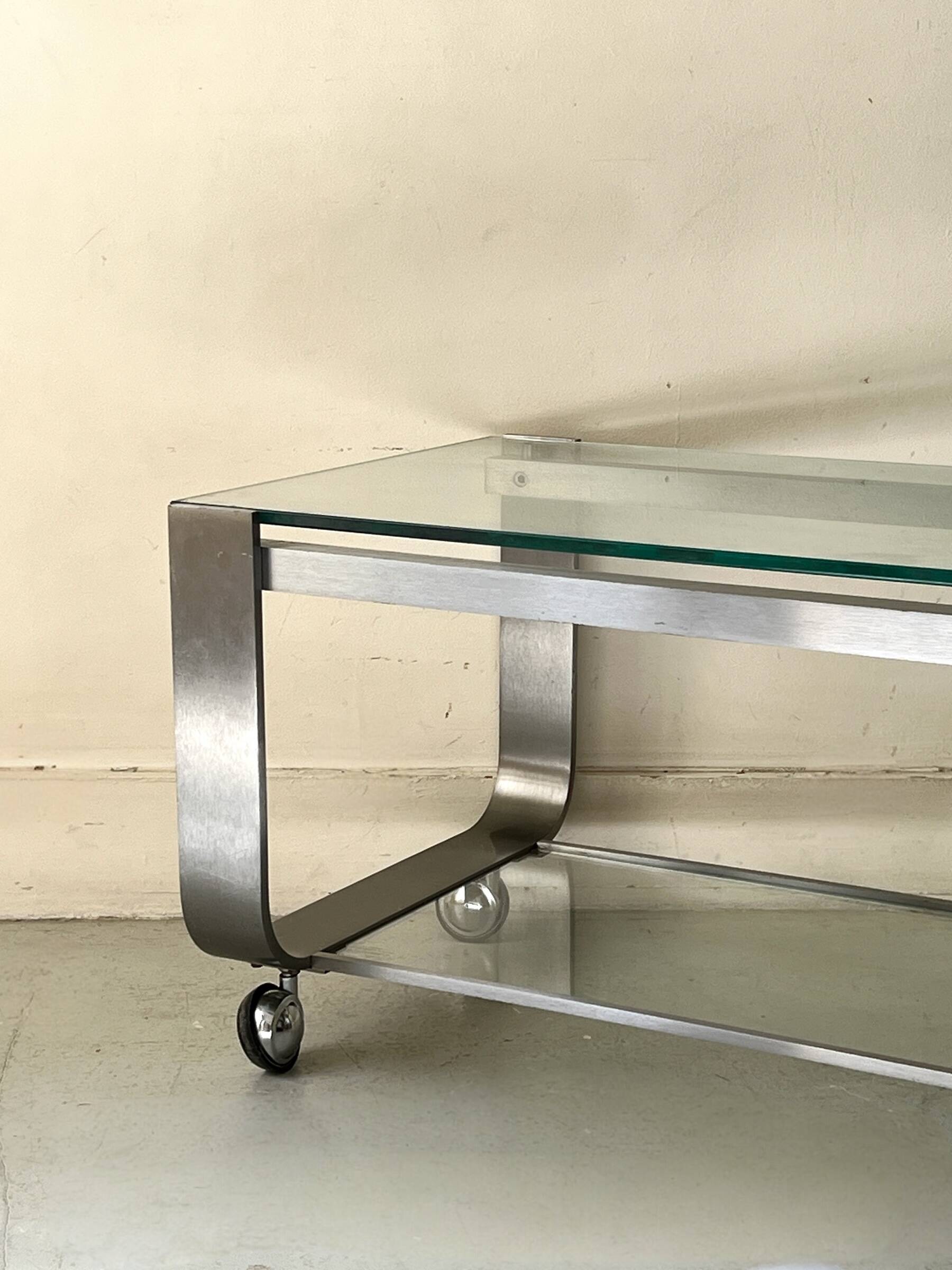 Brushed chrome coffee table with glass, 2 tiers on wheels, 1970s design.