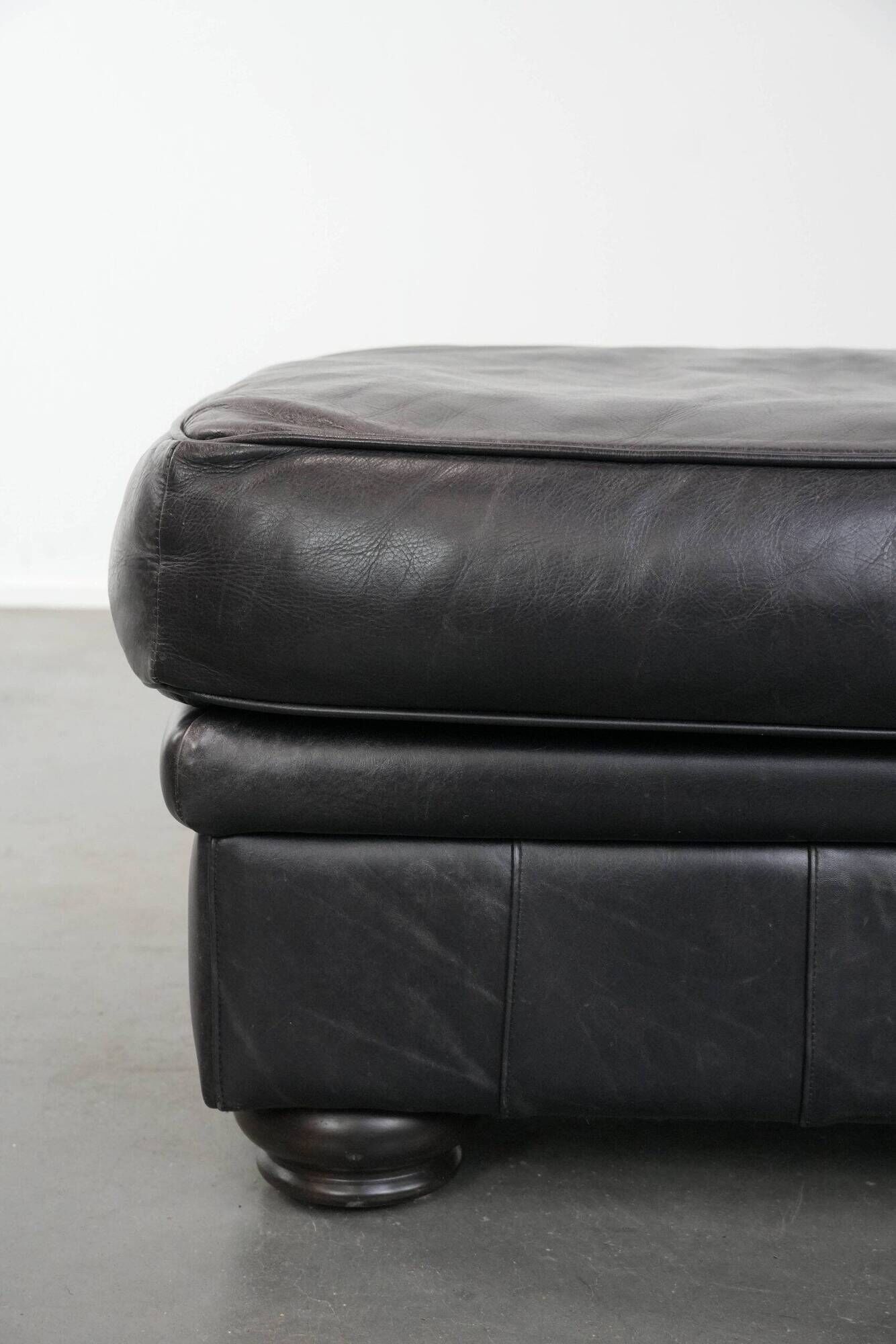 Set of a black cowhide leather Chesterfield armchair and matching ottoman
