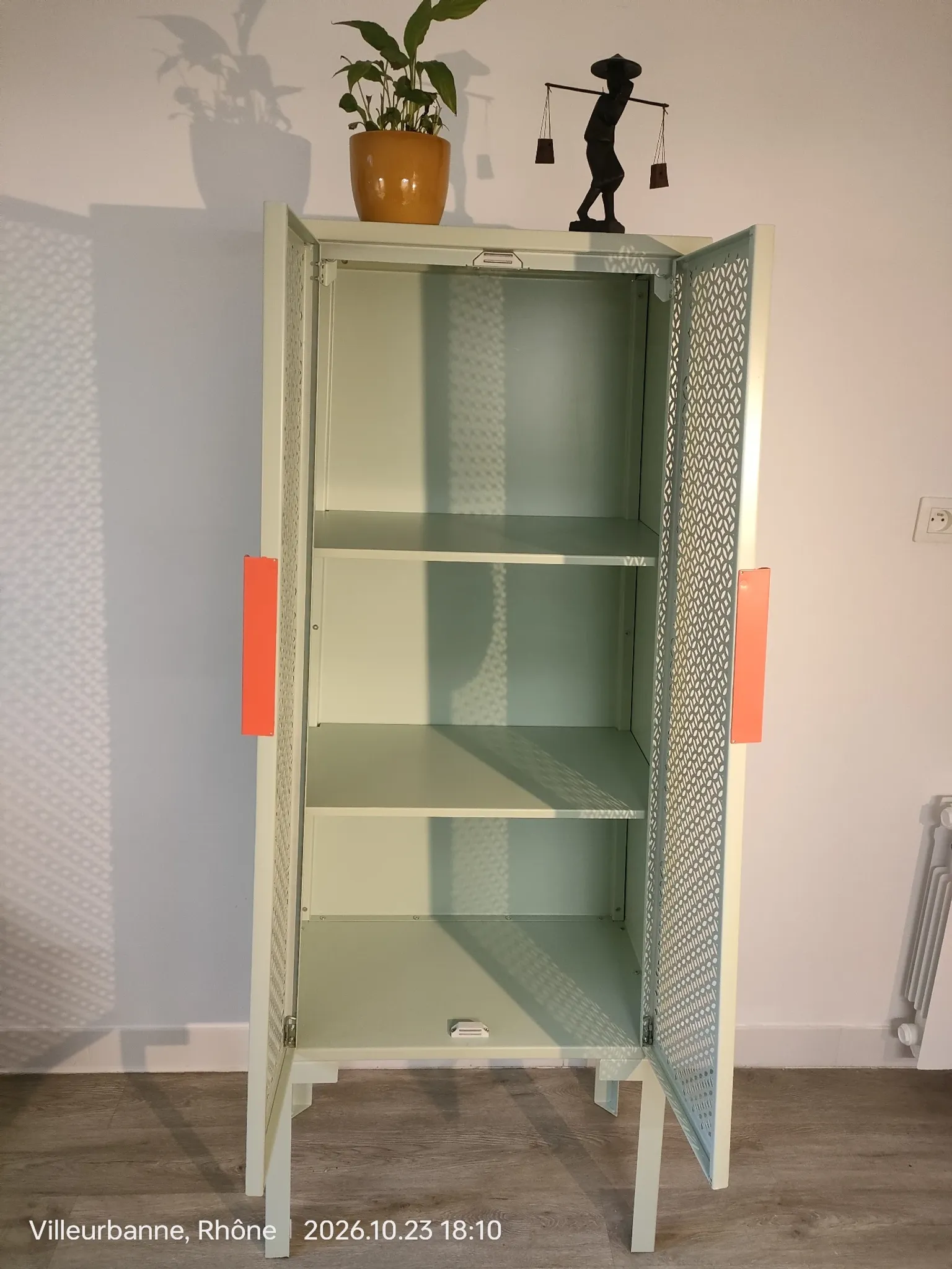 Vintage sage green metal wardrobe with louvered doors and coral handles.