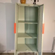 Vintage sage green metal wardrobe with louvered doors and coral handles.