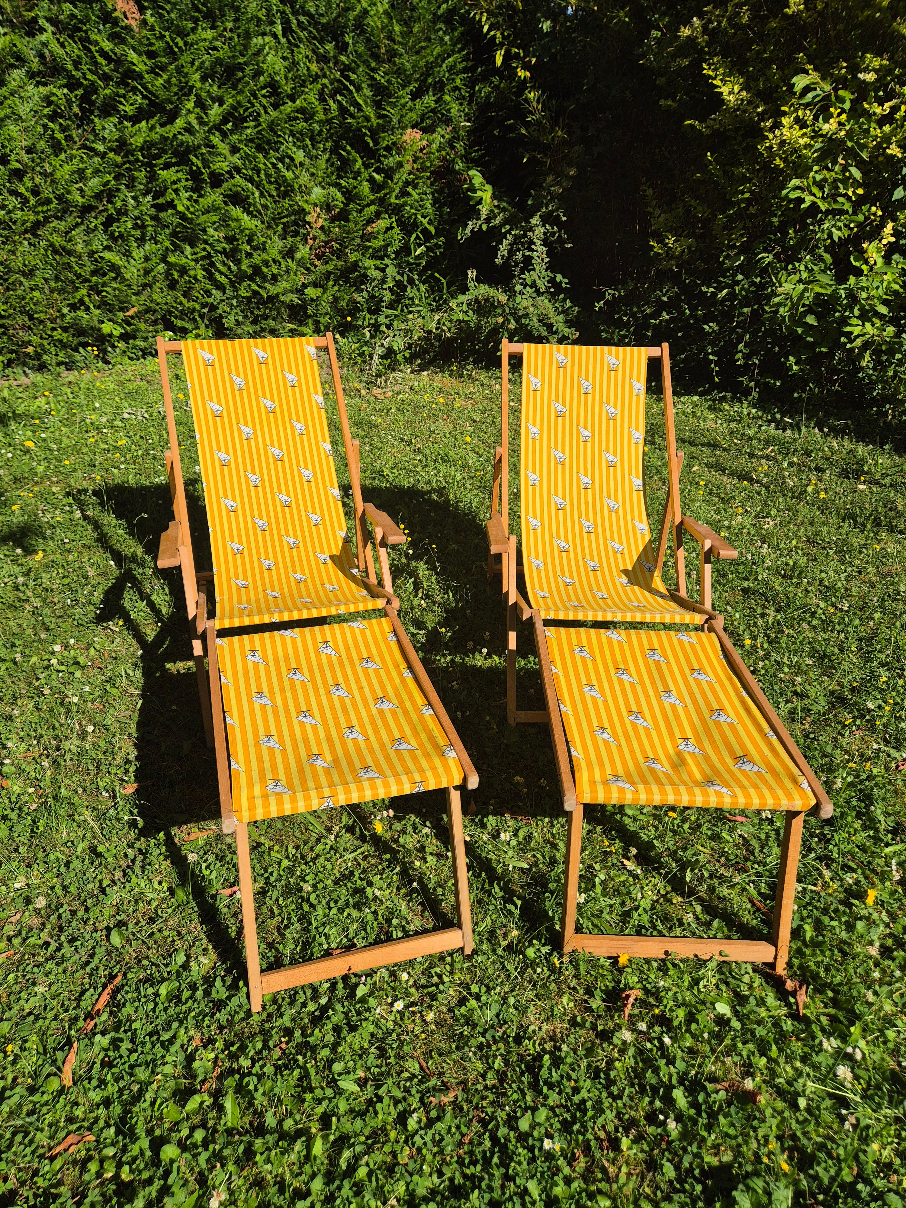 2 vintage Chilean deck chairs made of wood and yellow fabric printed with sailboats, with footrests.