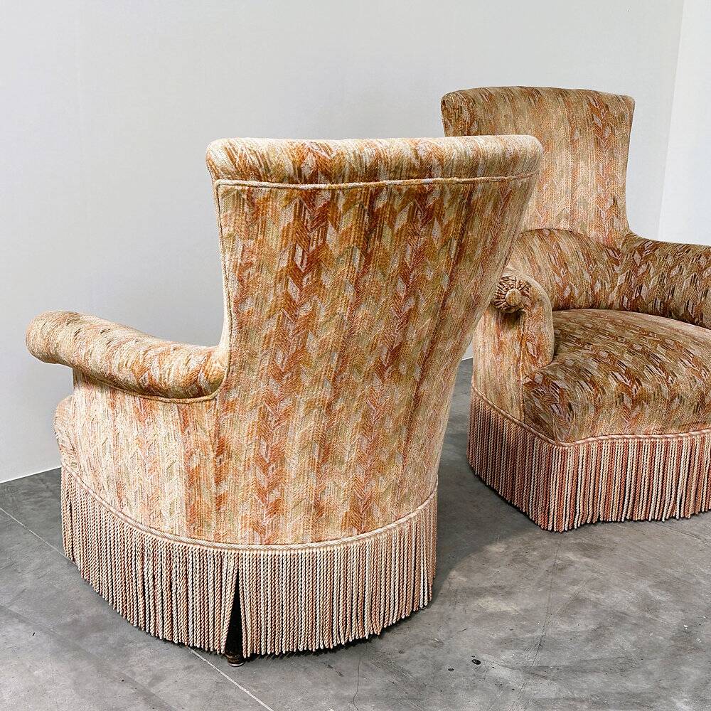 Pair of sculptural Hollywood Regency lounge chairs with original fringed upholstery