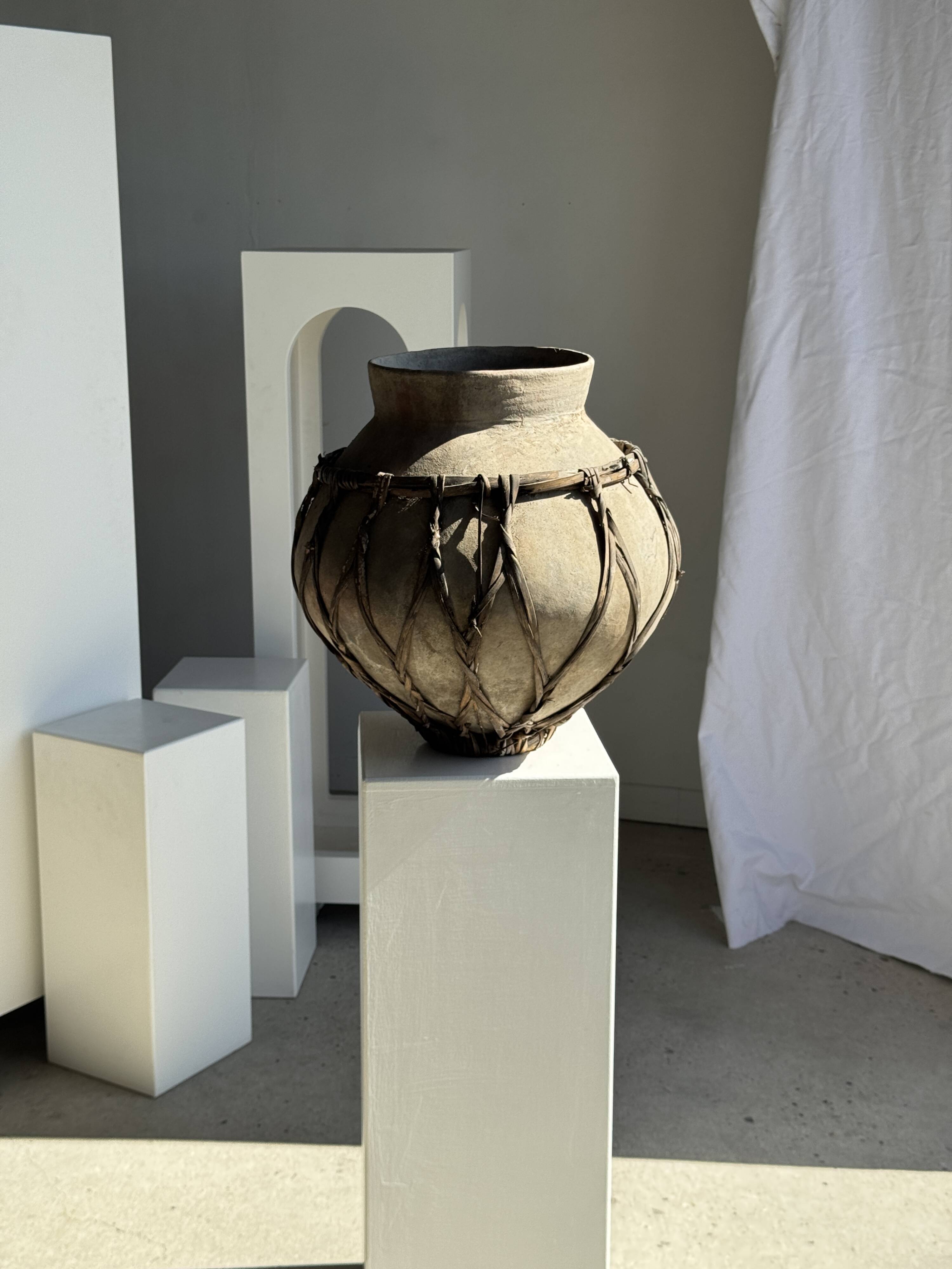 Very large light grey terracotta pot with handles and rattan crossbars.