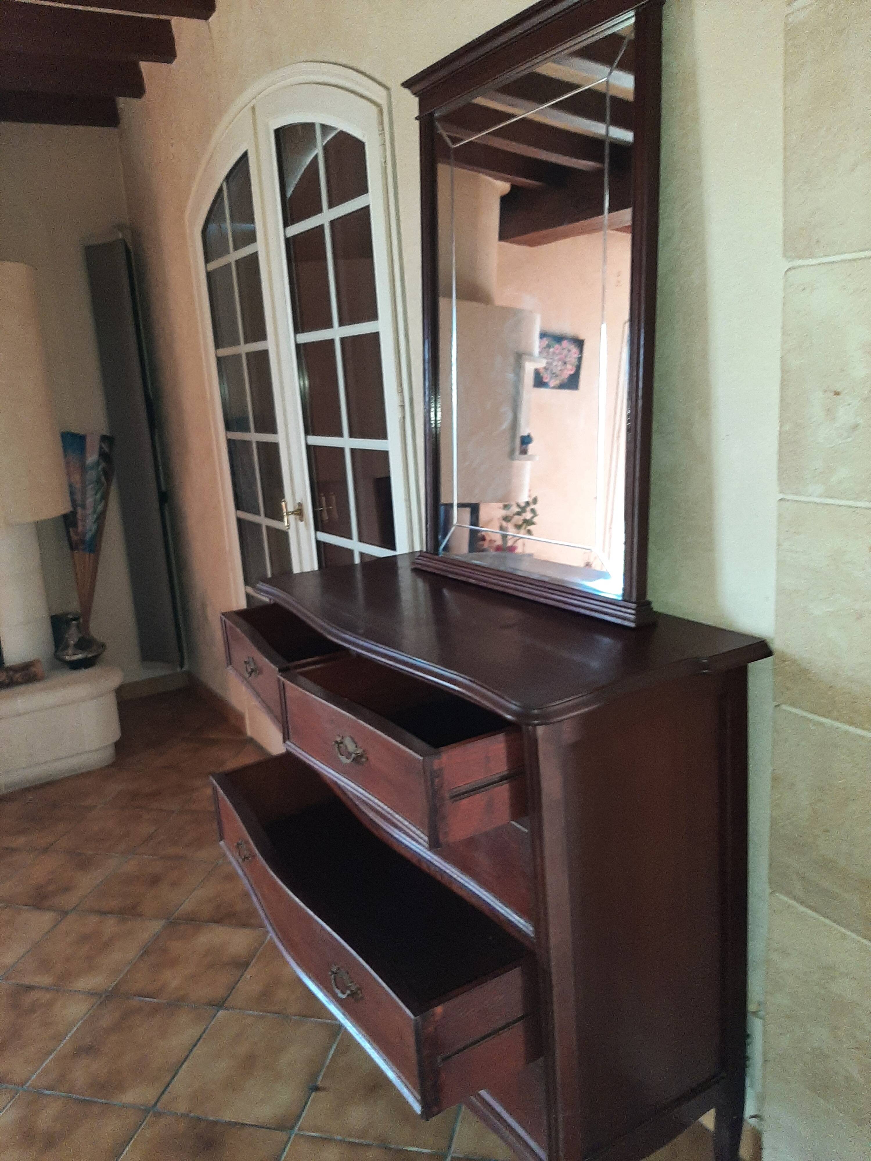Style set: bevelled mirror and curved wooden chest of drawers.