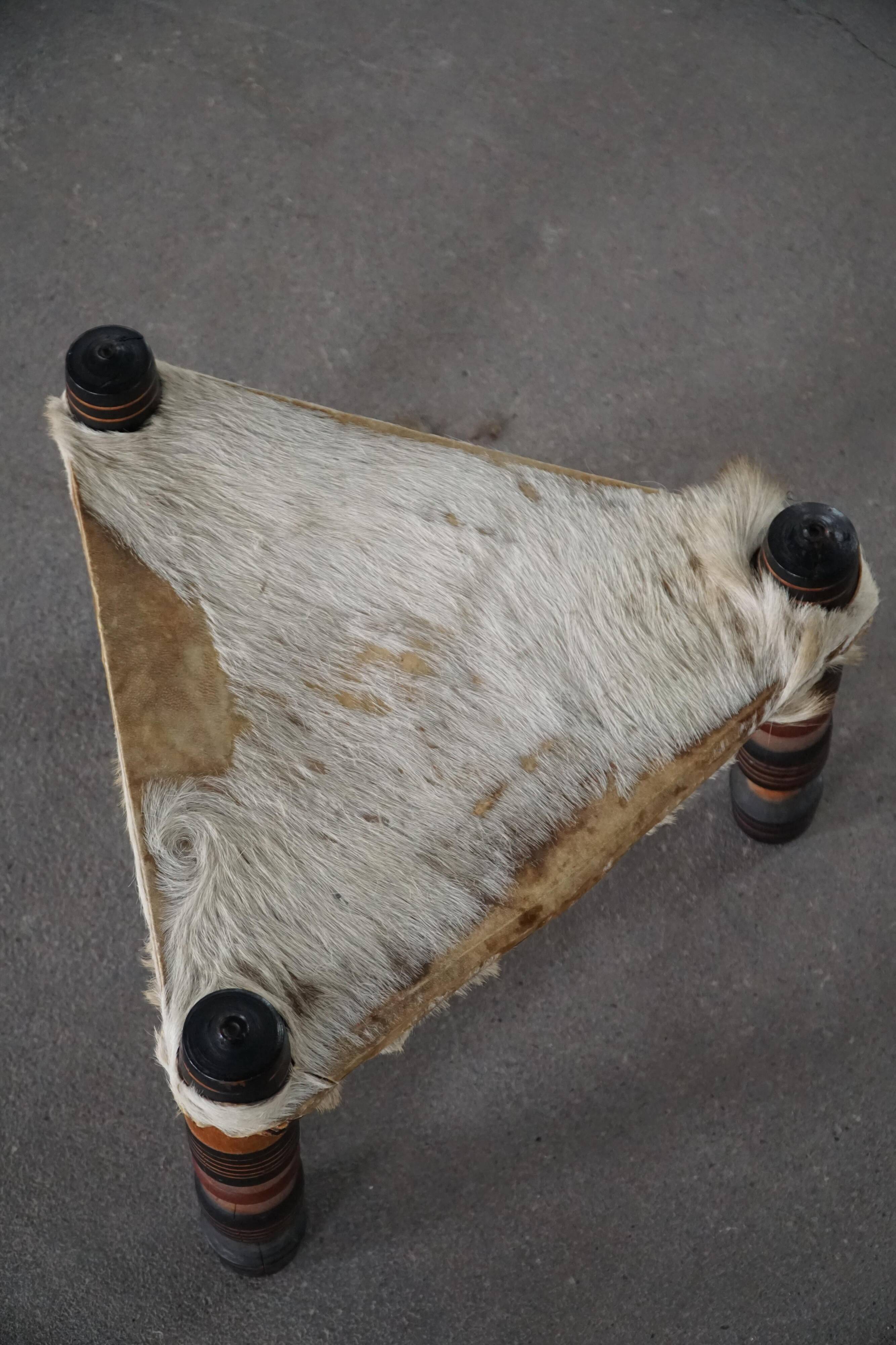 Vintage African artisanal stool, triangular shape with 3 legs, cowhide, 20th century.