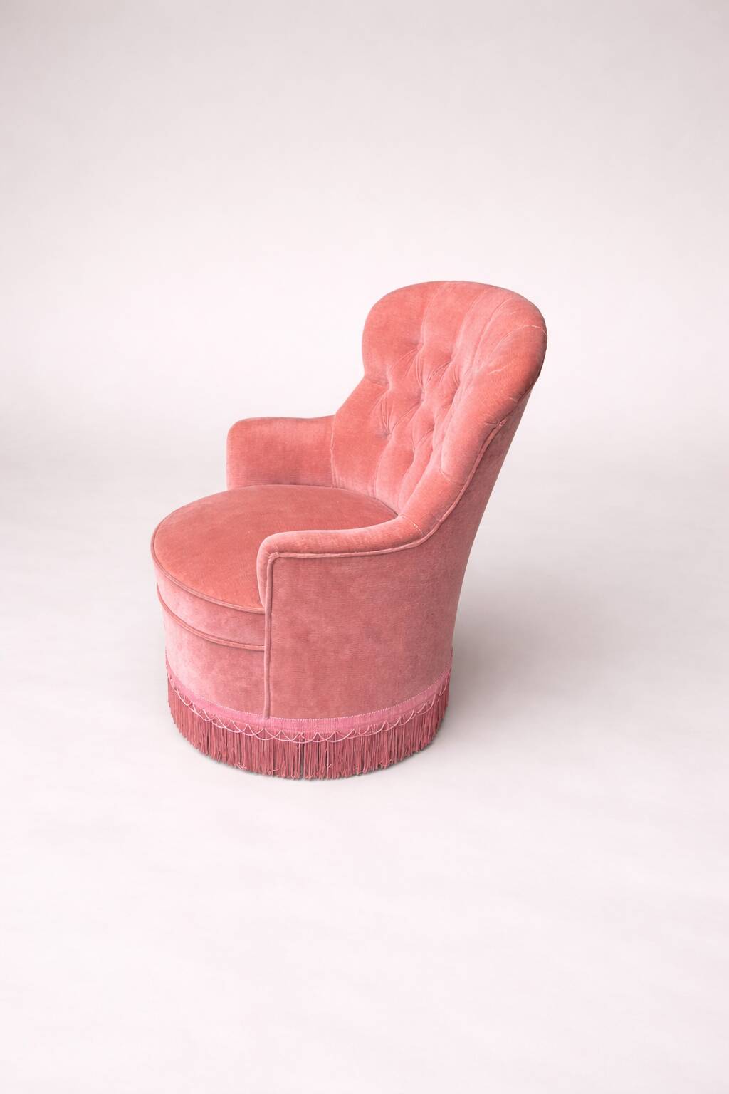Vintage pink velvet tufted armchair with fringes.