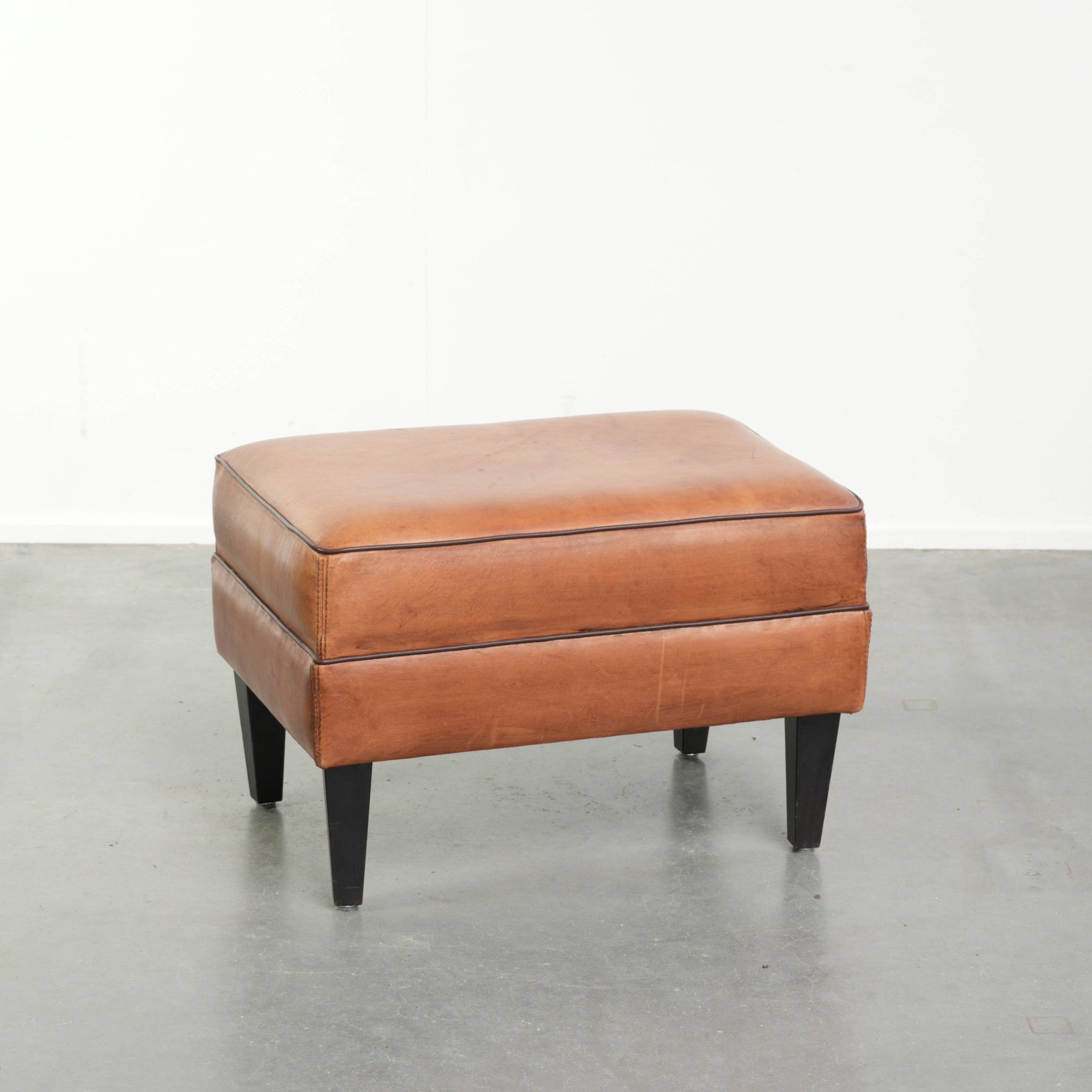 Handy sheepskin ottoman with warm colours finished with black piping